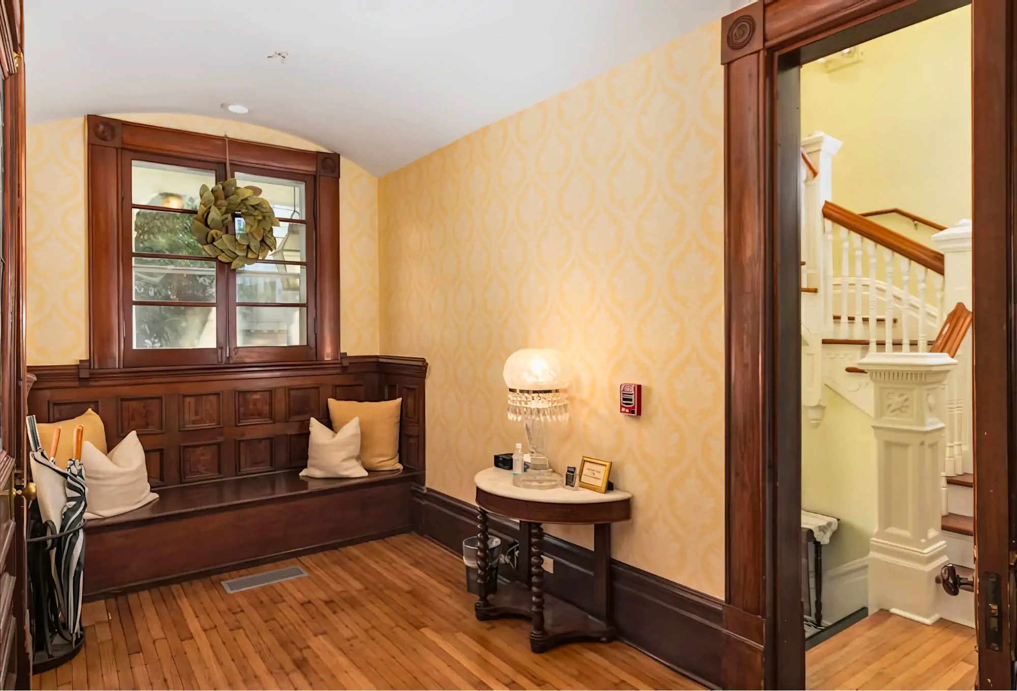 Welcoming entryway foyer with built-in wooden bench, yellow wallpaper, and beautiful woodwork in historic bed and breakfast