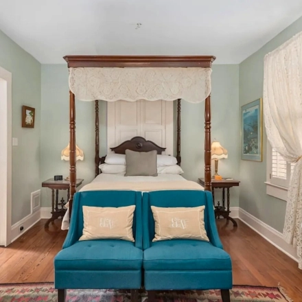  Mint green Victorian mansion with white columns, wraparound porch, manicured lawn and decorative black iron fence entrance 
