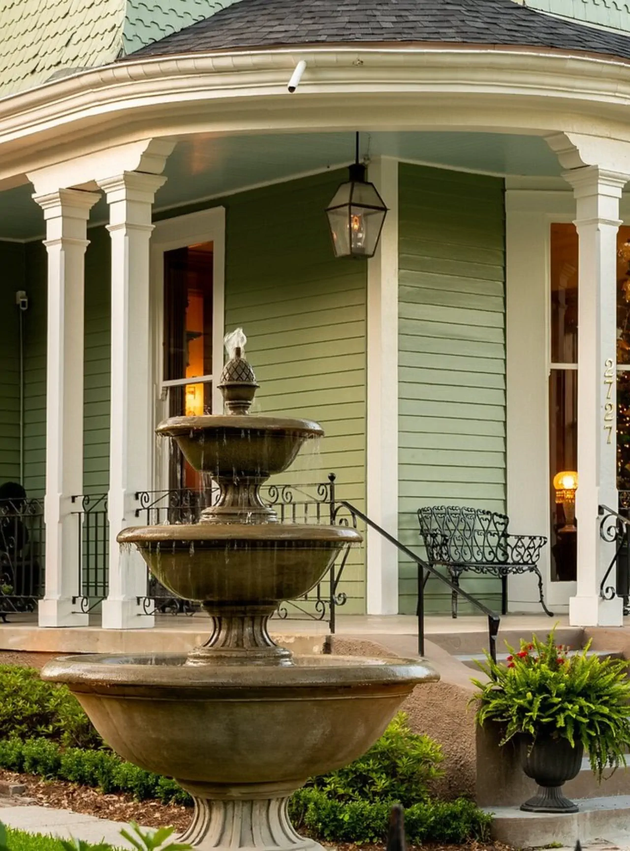 Detailed two-tier stone fountain on green Victorian home front porch