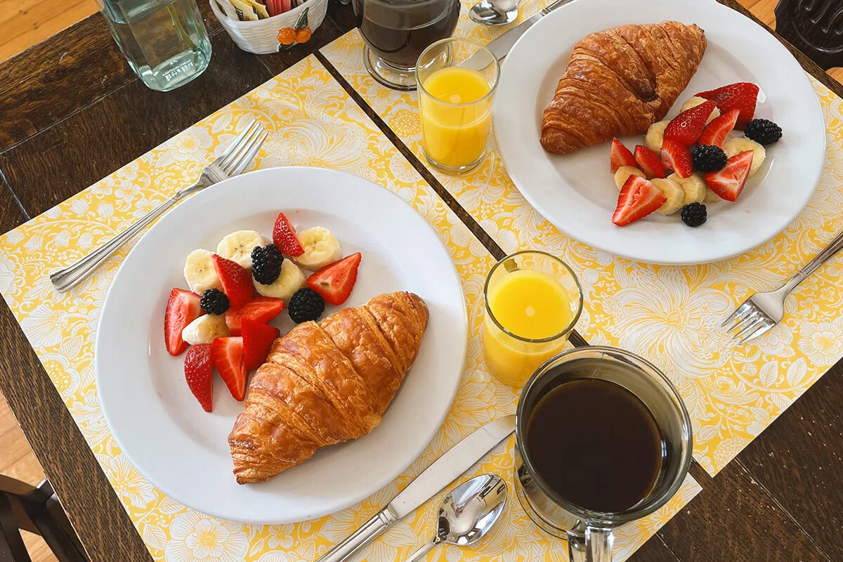  Elegant breakfast tray with croissant, fresh fruit, coffee, and orange juice on wrought iron patio furniture with garden view 